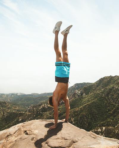 Adventurous man performing a handstand outdoors, against a backdrop of stunning views, embodying strength, balance, and a zest for life.