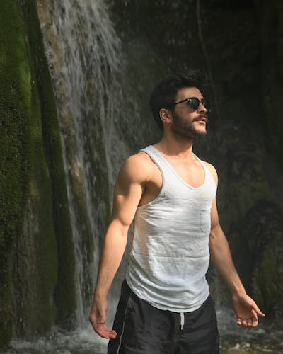 Confident man standing proudly in front of a waterfall, embodying strength and resilience amidst the breathtaking natural beauty.